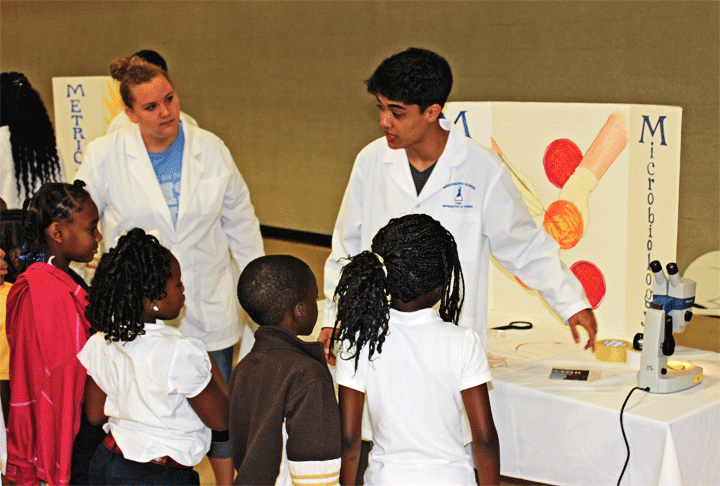 Class of 2015 students Savannah Culver and Jacob Sheward present the wonders of microscope viewing to a cluster of local elementary students at the 2014 Science Carnival. 