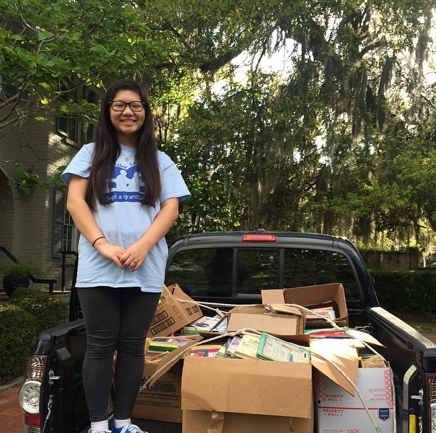 Jenny Nguyen standing next to 1,200 books collected for Little Bookworms.