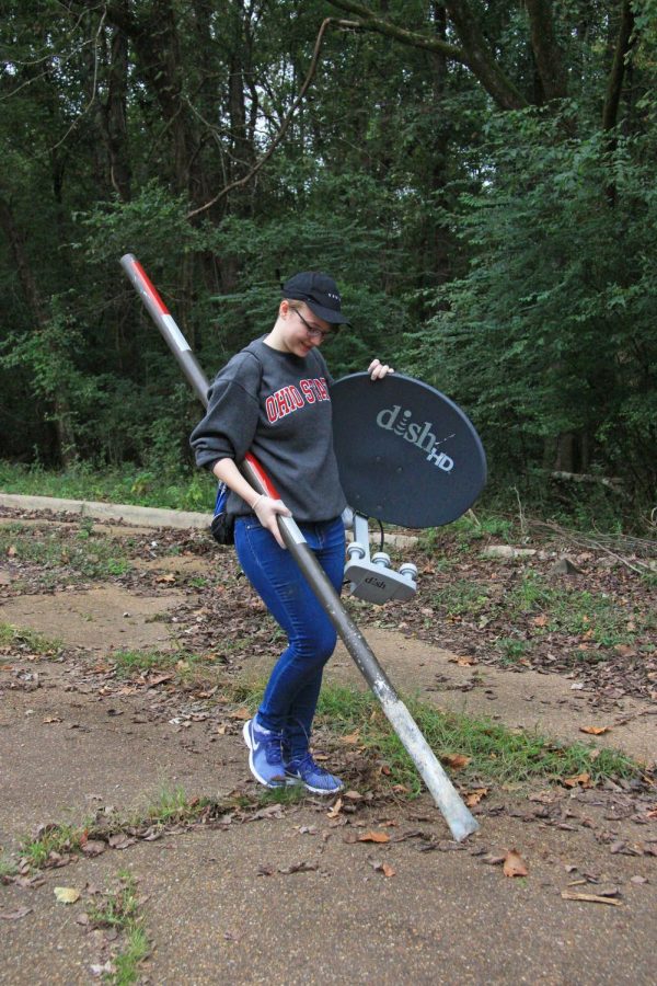 Millie Perdue carries a metal pole and a satellite dish back to the piles of trash.