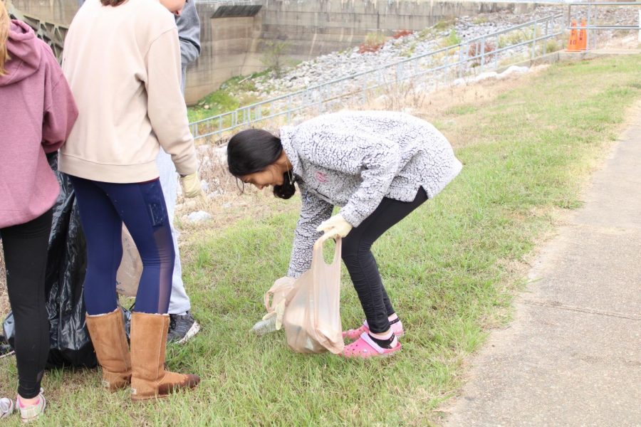 Kresha Patel leans over to pick up a soda can and plastic bag.