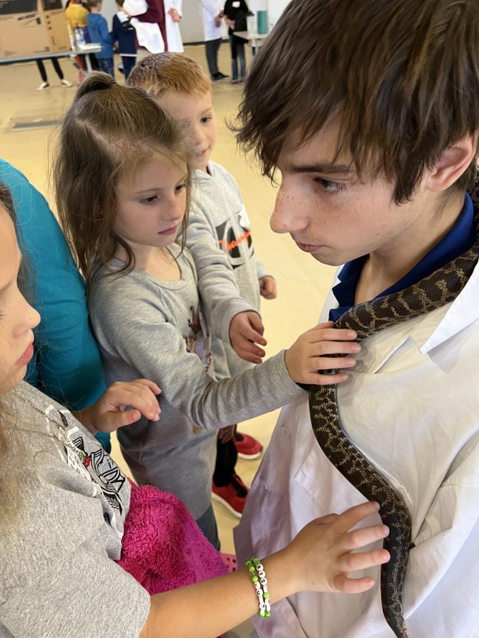 Young students watch a snake crawling on junior Sebastian Harvey at the MSMS Science Carnival.