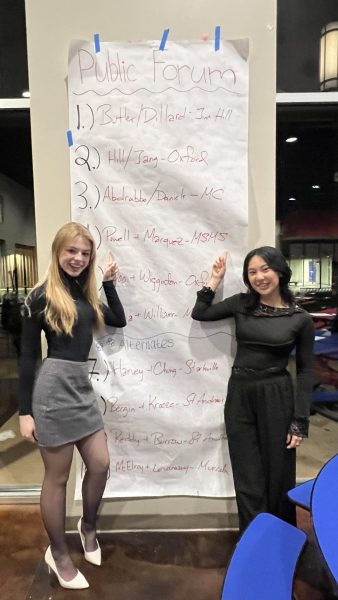 Seniors Mariane Powell (left) and Lucianna Marquez point to their names on the National Catholic Forensic League Public Forum qualifiers list from the Junior Catholic Forensic League tournament on Feb. 9-10.